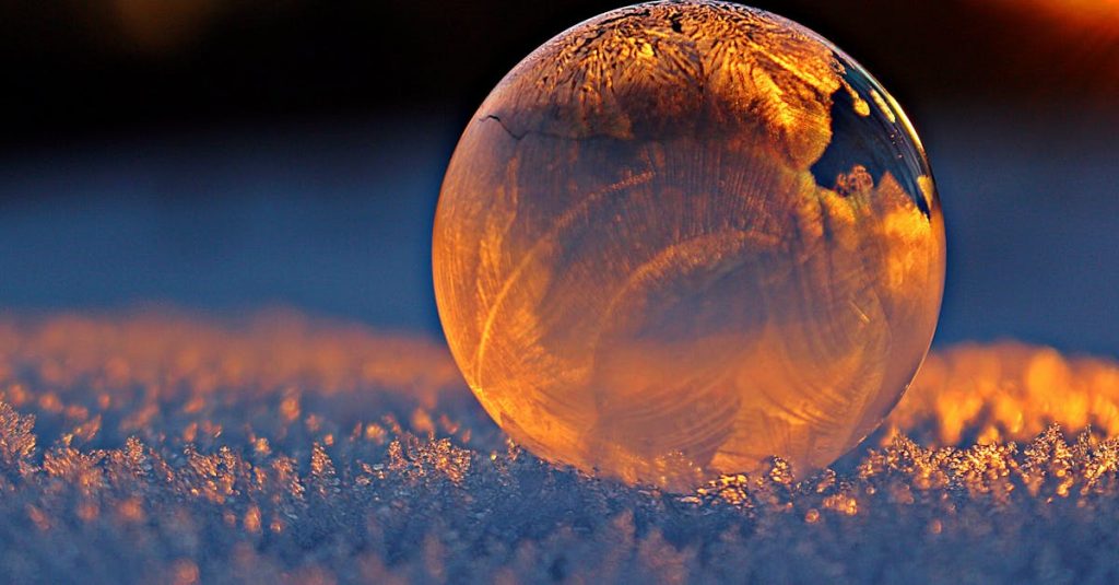 Close-up shot of a frozen bubble with warm reflections resting on a snowy surface at twilight.